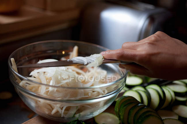 Cropped image of woman holding knife above bowl of freshly sliced onion — Stock Photo