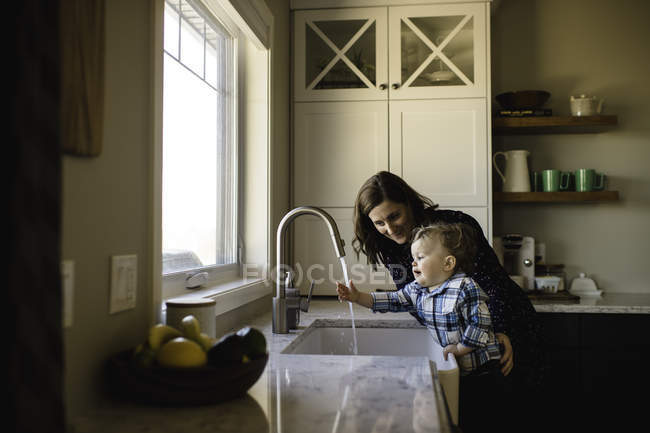 Mother helping toddler son wash hands at kitchen sink — Stock Photo