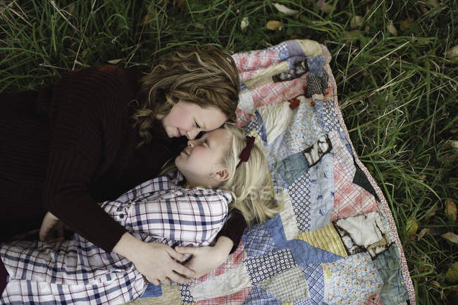 Mother and daughter lying on blanket face to face hugging — Stock Photo