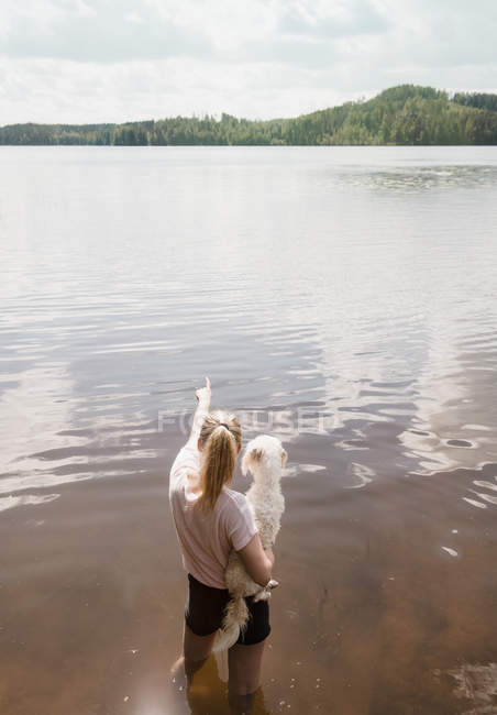 Donna in piedi nel lago che trasporta il cane coton de tulear, Orivesi, Finlandia — Foto stock
