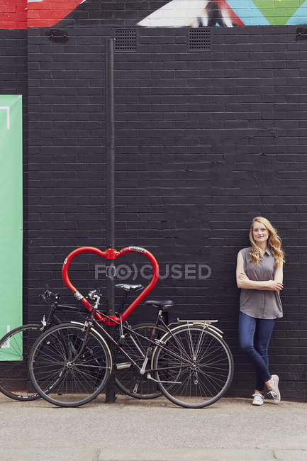 Woman leaning against wall beside bicycle stand — Stock Photo