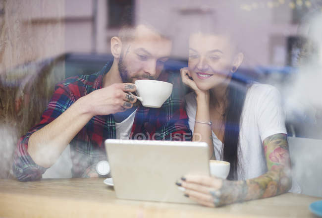 View through window of couple in coffee shop using digital tablet — Stock Photo