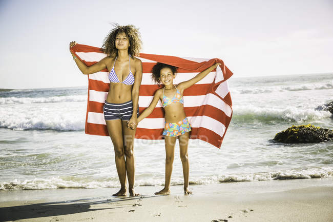 Madre e hija sosteniendo toalla en la playa - foto de stock
