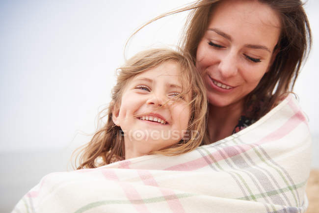 Happy mother and daughter wrapped in blanket — Stock Photo