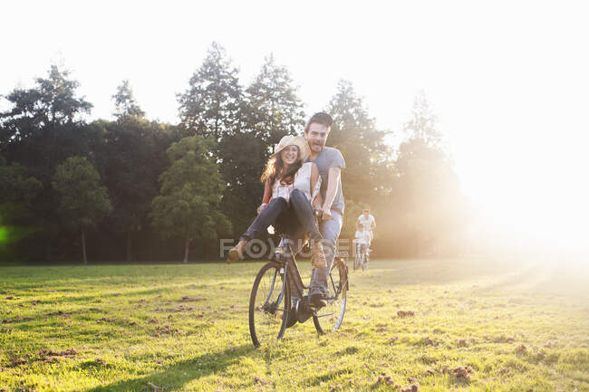 Молода жінка на кермі велосипеда хлопців на вечірці в парку — стокове фото