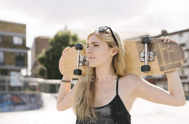 Young female skateboarder carrying skateboard on shoulders in skatepark — Stock Photo