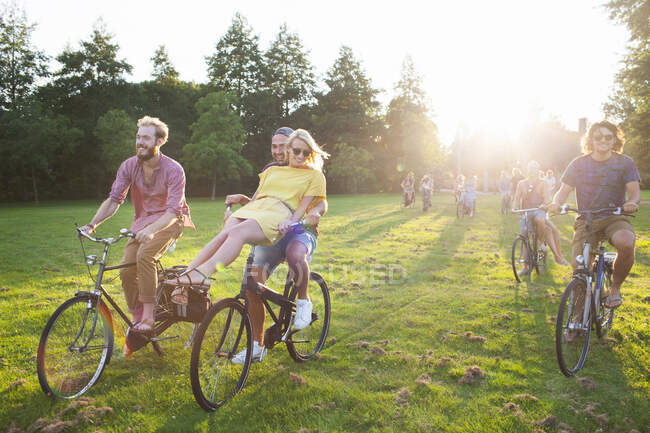 Multitud de adultos de fiesta que llegan en bicicletas a la fiesta del parque del atardecer - foto de stock
