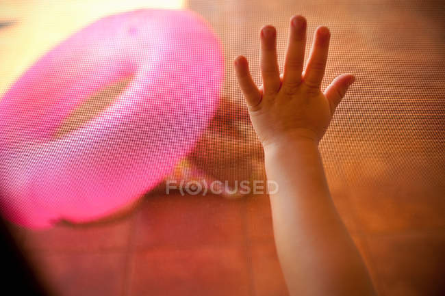 Mão da criança tocando tela de malha, anel inflável rosa no fundo — Fotografia de Stock