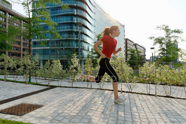 Молодая женщина бежит мимо офисных зданий — стоковое фото