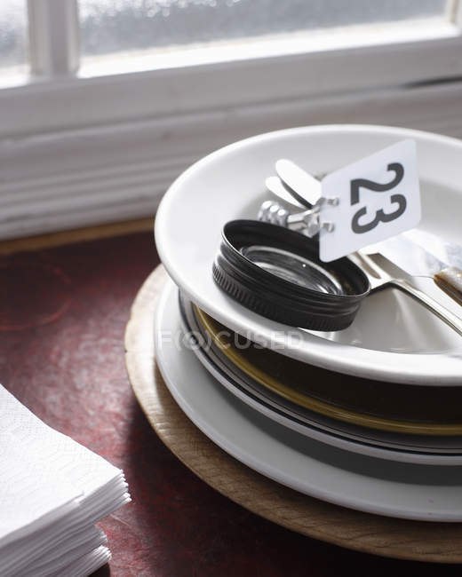 Pila di piatti, segno con il numero 23 e tovaglioli sul davanzale della finestra nel ristorante — Foto stock