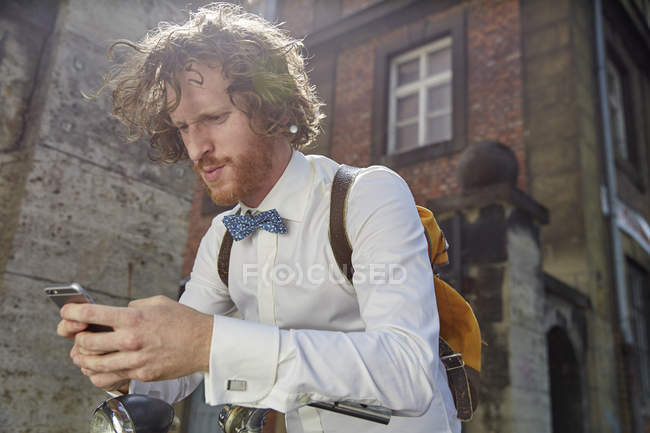 Молодой человек на улице, с помощью смартфона, в рубашке и бабочке — стоковое фото