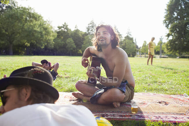 Дорослі друзі грають на акустичній гітарі на вечірці парку заходу сонця — стокове фото