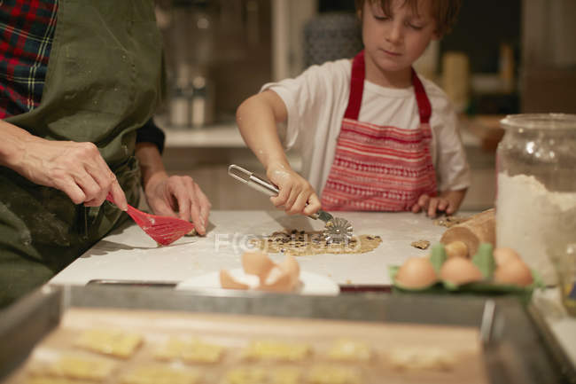 Cropped shot of woman and son cutting dough on kitchen counter — Stock Photo