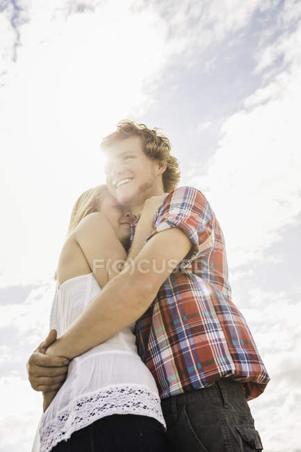 Joven abrazando novia contra el cielo iluminado por el sol - foto de stock
