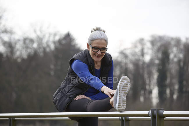Woman with leg raised on railing bending forward stretching — Stock Photo