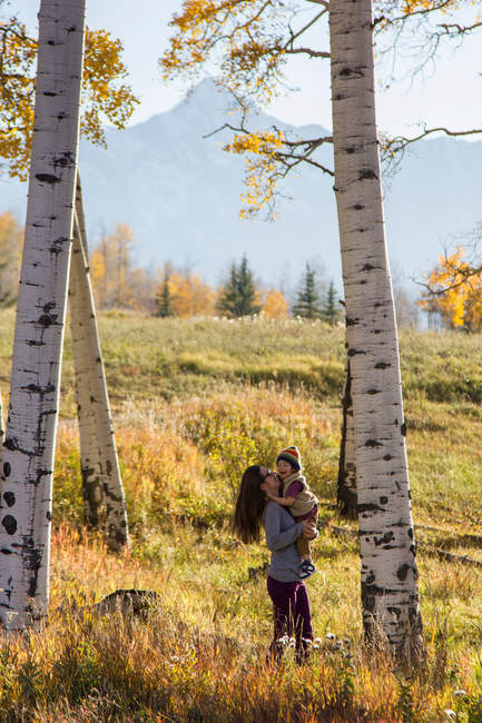 Mother holding toddler amongst autumnal silver birch trees — Stock Photo