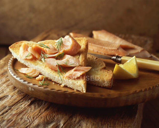 Лосось на тості з кропом і лимонним шматочком на дерев'яній дошці — стокове фото