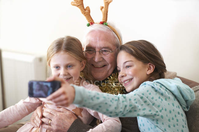 Сестри беруть смартфон селфі з дідусем в оленячих ролях — стокове фото