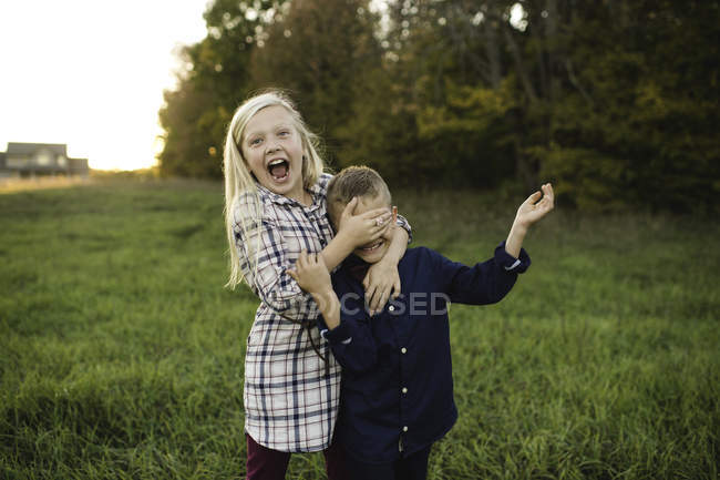 Schwester bedeckt lächelnd Bruders Augen — Stockfoto