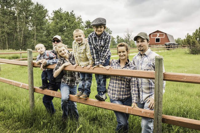 Mehrgenerationenfamilie steht hinter Zaun auf Bauernhof und blickt lächelnd in Kamera — Stockfoto