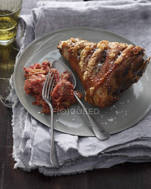 Roasted ham hock with garnish and cutlery on plate — Stock Photo