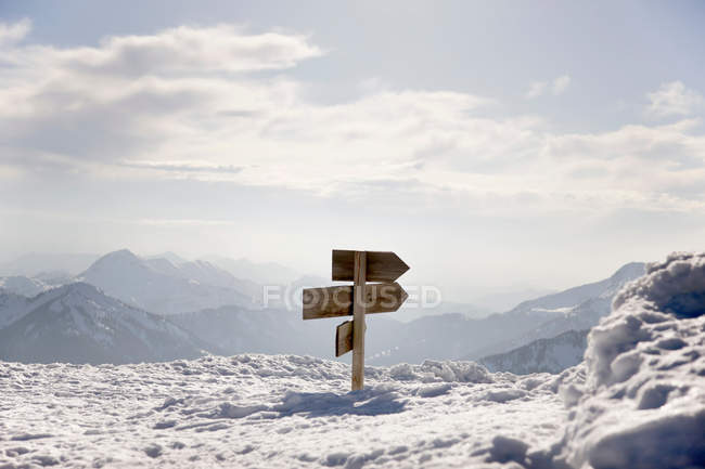 Letrero de flechas de madera en montañas cubiertas de nieve - foto de stock