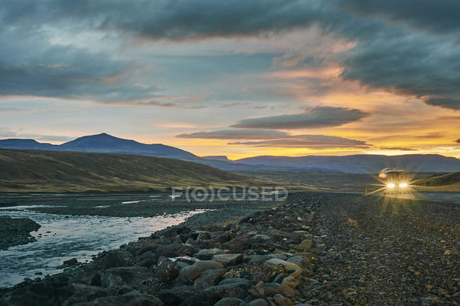 Faróis de carro ao pôr do sol na paisagem da montanha — Fotografia de Stock