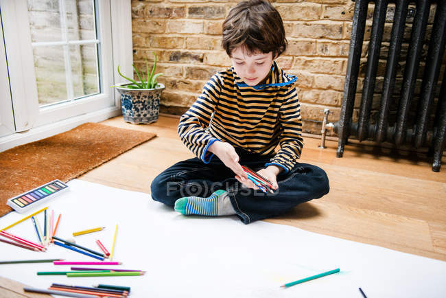 Niño sentado en el suelo dibujo en papel largo - foto de stock