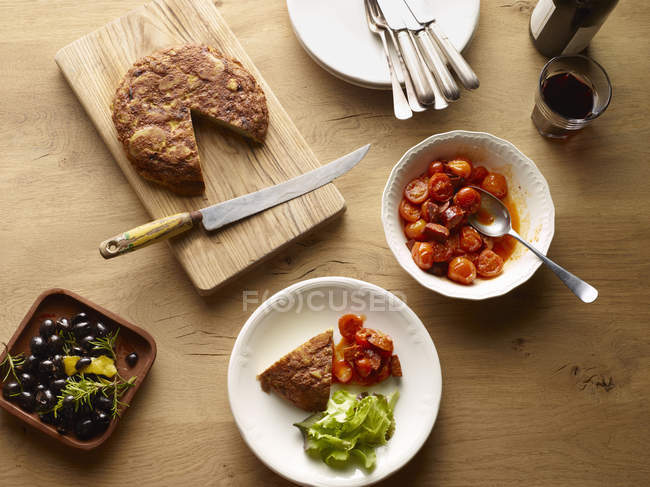 Vista superior da mesa com tortilla de batata espanhola e tigela de tomates — Fotografia de Stock