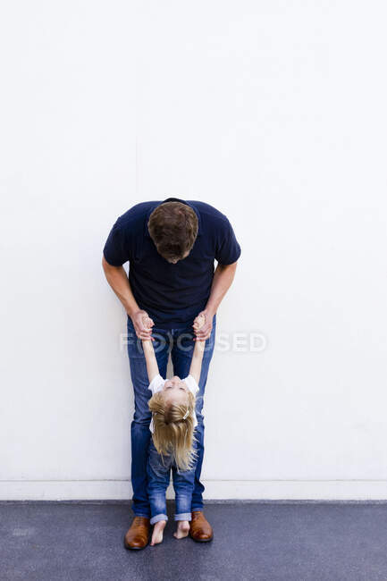 Retrato de un hombre maduro con una hija inclinada hacia atrás frente a una pared blanca - foto de stock