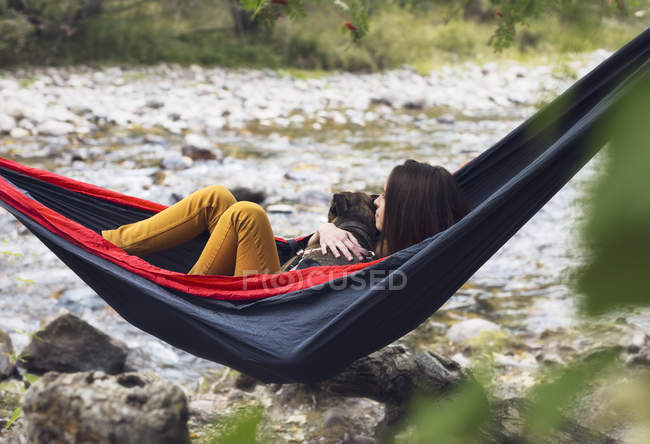 Young woman relaxing in hammock with dog, outdoors — Stock Photo