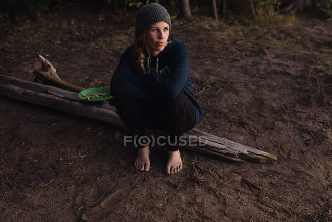 Середня доросла жінка сидить на дереві в лісі, дивлячись геть — стокове фото