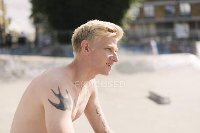 Татуйований молодий чоловік скейтбордист сидить у скейтпарку — стокове фото