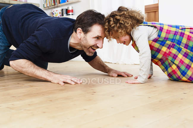 Зрелый мужчина ползает голова к голове с дочерью на полу на кухне — стоковое фото