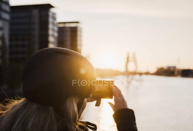 Woman taking photograph of Molecule Man sculpture at sunset, Spree River, Berlin, Germany — Stock Photo