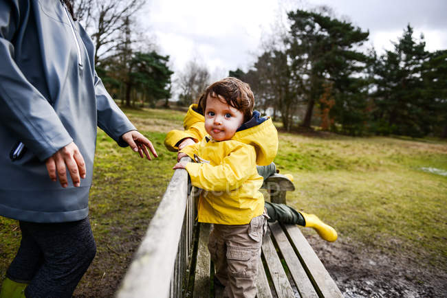 Baby boy with mother in yellow anorak on park bench — Stock Photo
