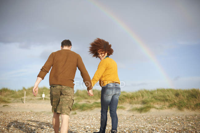 Coppia a piedi sulla spiaggia verso arcobaleno — Foto stock
