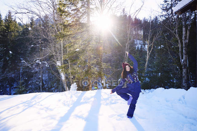 Woman in winter clothes practicing tree yoga pose in snow by forest, Austria — Stock Photo