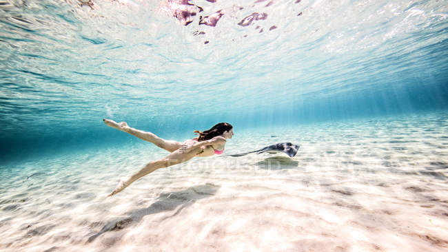 Свободный дайвер-женщина плавает со скатом возле морского дна — стоковое фото