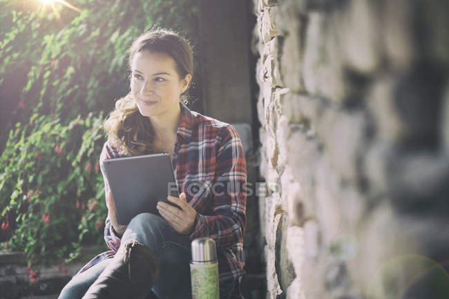 Mujer adulta que usa tableta digital en jardines en Thornbury Castle, South Gloucestershire, Reino Unido - foto de stock