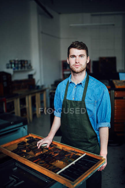 Ritratto di giovane artigiano accanto al vassoio di lettere tipografiche in laboratorio di stampa — Foto stock