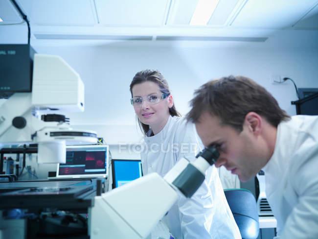 Científicos en batas de laboratorio usando microscopio láser - foto de stock