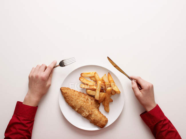 Вид сверху на руки по тарелке рыбы и чипсов — стоковое фото
