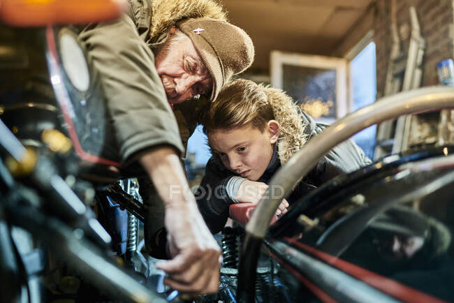 Motociclista masculino sênior explicando a manutenção da motocicleta para o neto na garagem — Fotografia de Stock