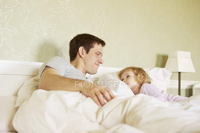 Niña y padre mirándose en la cama - foto de stock