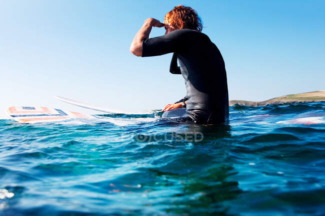 Hombre sentado en la tabla de surf en el agua - foto de stock