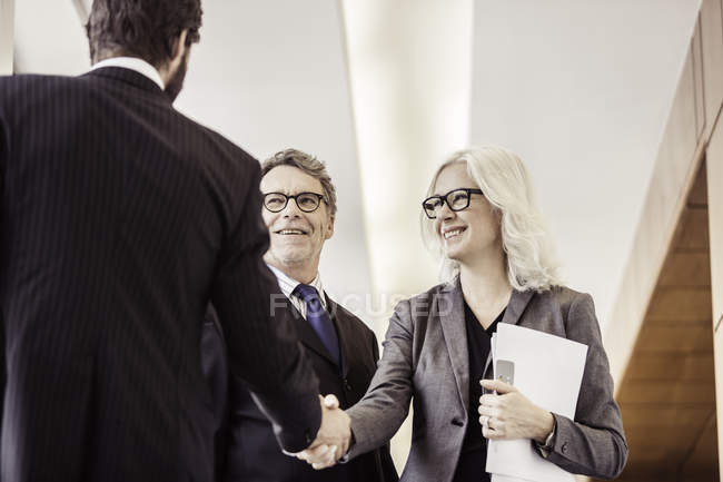 Businessmen and woman shaking hands in office corridor — Stock Photo