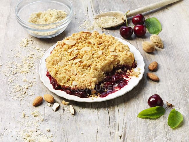 Cherry and almond crumble pudding on messy table — Stock Photo