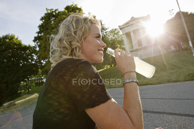 Mid adult woman in sunlit park drinking lemonade — Stock Photo