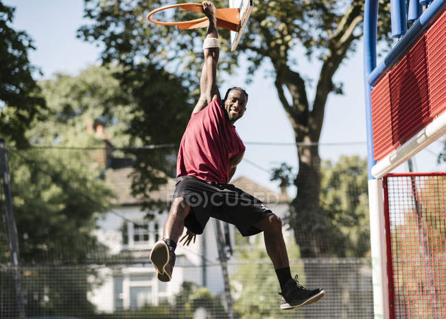 Porträt eines jungen männlichen Basketballspielers, der am Basketballkorb hängt — Stockfoto